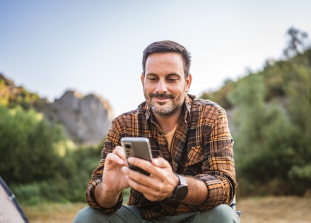 A man sitting in front of a tent using his mobile phone on a camping trip