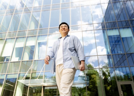 Businessman walking outside of an office building in Malaysia holding a laptop