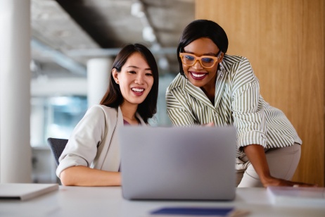 Dos mujeres sonriendo y hablando sobre el cumplimiento global de RR. HH. y mirando la pantalla de un ordenador.