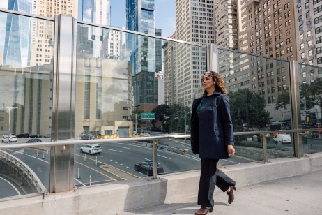 Una mujer de traje, caminando por un puente sobre una carretera rodeada de edificios de oficinas