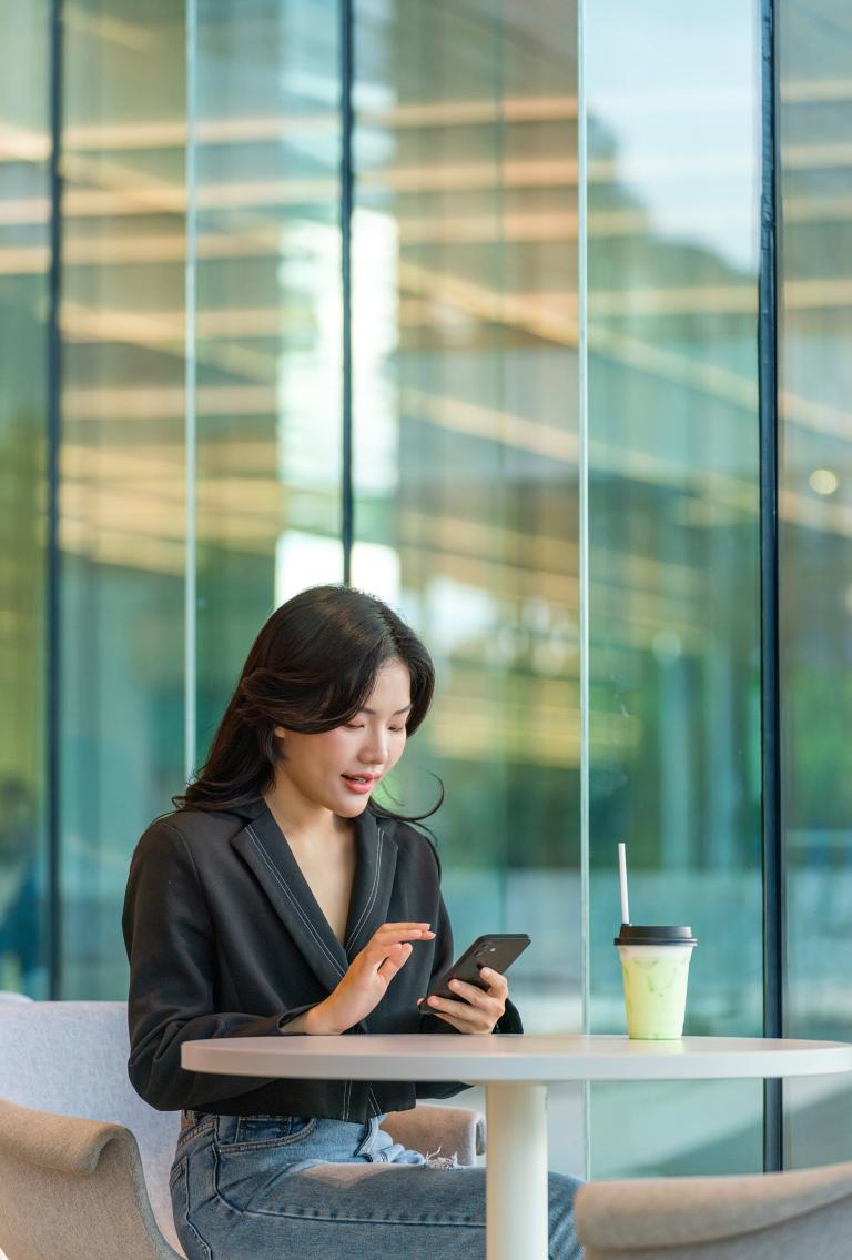 Una chica sentada en una mesa con un café y buscando Pebl EOR en internet con su teléfono móvil.