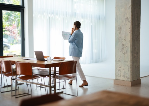Remote employee takes a call while looking at print out of charts in her well-lit home. 