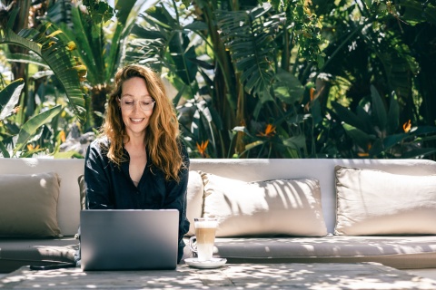Smiling woman working on laptop outdoors in tropical garden