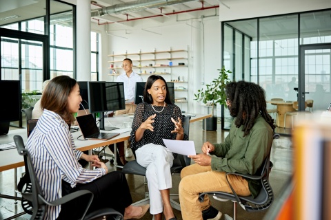 Three colleagues sitting in chairs discussing workplace culture in Qatar