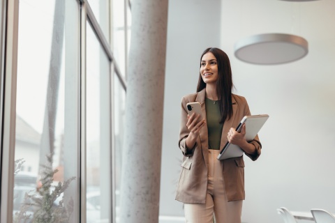 Young businesswoman walking in modern office holidaying a laptop and smartphone
